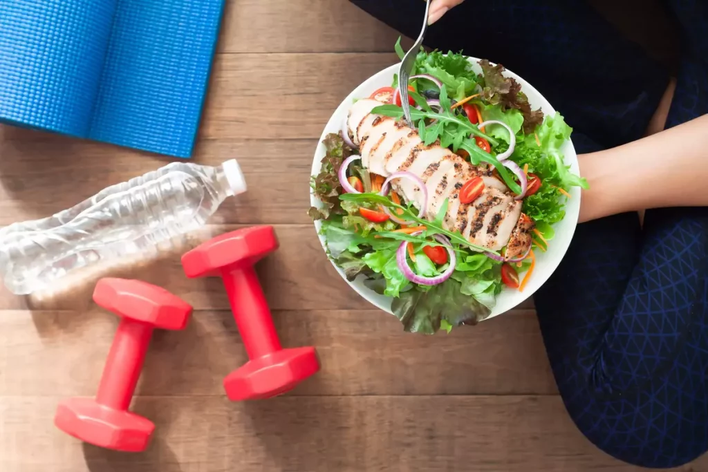 Woman holding a salad next to dumbells and a water bottle